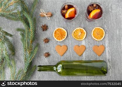 christmas and seasonal drinks concept - hot mulled wine, empty green glass bottle, dry orange slices, gingerbread and aromatic spices on grey background. mulled wine, orange slices, gingerbread and spices