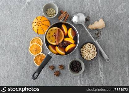 christmas and seasonal drinks concept - pot with hot mulled wine, orange slices, aromatic spices, nuts and ladle on grey background. pot with hot mulled wine, orange slices and spices