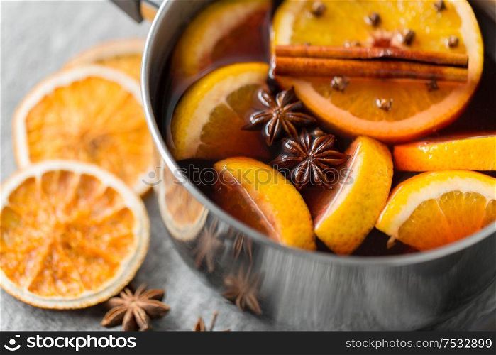 christmas and seasonal drinks concept - pot with hot mulled wine, orange slices and aromatic spices on grey background. pot with hot mulled wine, orange slices and spices