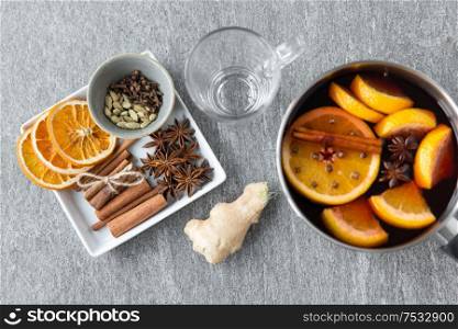 christmas and seasonal drinks concept - pot with hot mulled wine, orange slices, aromatic spices and glass mug on grey background. pot with hot mulled wine, orange slices and spices