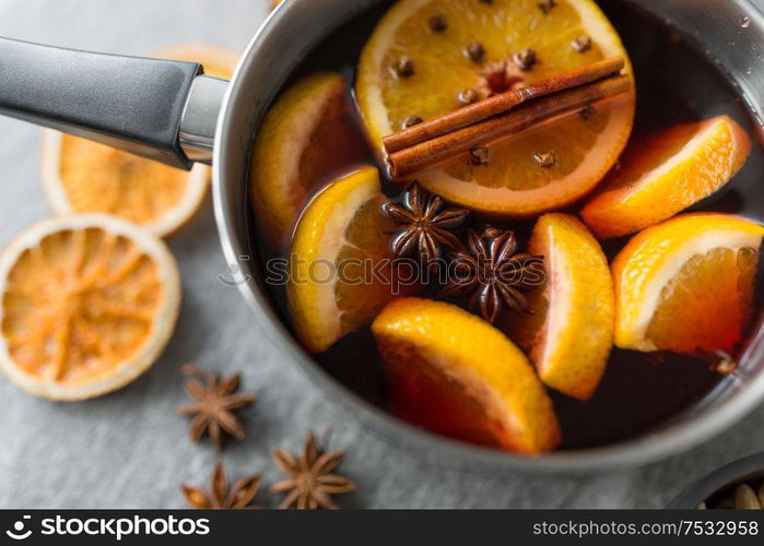 christmas and seasonal drinks concept - pot with hot mulled wine, orange slices and aromatic spices on grey background. pot with hot mulled wine, orange slices and spices