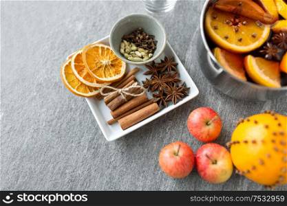 christmas and seasonal drinks concept - pot with hot mulled wine, orange slices, aromatic spices and apples on grey background. pot of hot mulled wine, orange, apples and spices