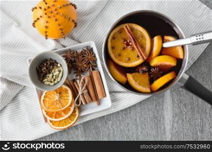 christmas and seasonal drinks concept - pot with hot mulled wine, orange slices, aromatic spices and ladle on grey background. pot with hot mulled wine, orange slices and spices