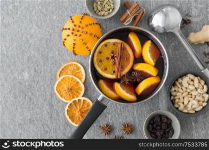christmas and seasonal drinks concept - pot with hot mulled wine, orange slices, aromatic spices, nuts and ladle on grey background. pot with hot mulled wine, orange slices and spices