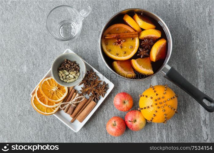christmas and seasonal drinks concept - pot with hot mulled wine, orange slices, aromatic spices and glass mug on grey background. pot with hot mulled wine, orange slices and spices
