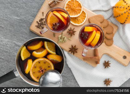 christmas and seasonal drinks concept - pot with hot mulled wine, orange slices, aromatic spices and ladle on grey background. pot with hot mulled wine, orange slices and spices