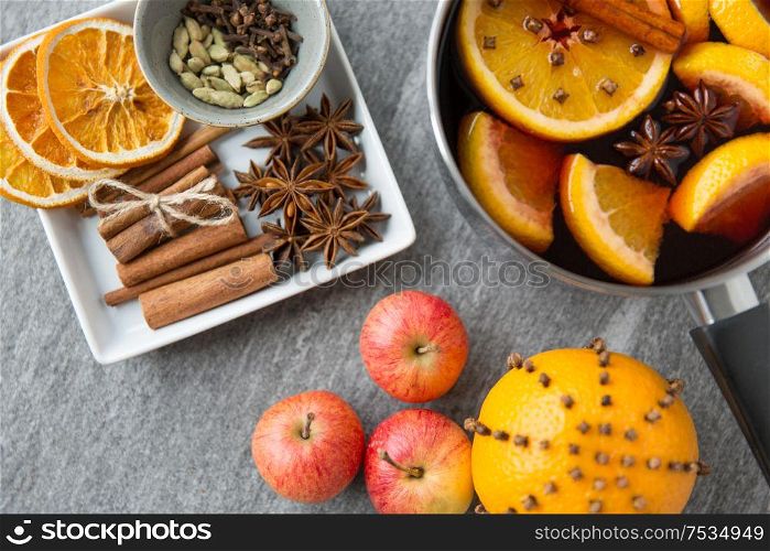 christmas and seasonal drinks concept - pot with hot mulled wine, orange slices, aromatic spices and apples on grey background. pot of hot mulled wine, orange, apples and spices
