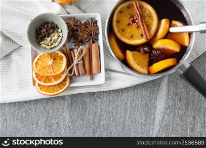christmas and seasonal drinks concept - pot with hot mulled wine, orange slices, aromatic spices and ladle on grey background. pot with hot mulled wine, orange slices and spices