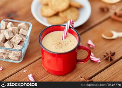 christmas and seasonal drinks concept - red cup of eggnog with candy cane, oatmeal cookies, fir tree branches and sugar on wooden background. cup of eggnog with candy cane, cookies and sugar