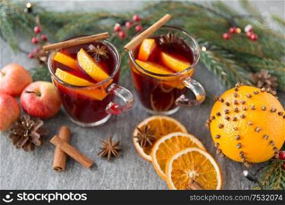 christmas and seasonal treats concept - glass of hot mulled wine with orange slice, apples and fir branch on grey background. glass of hot mulled wine, cookies, apples and fir
