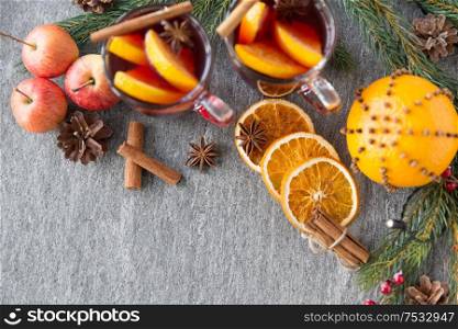 christmas and seasonal treats concept - glass of hot mulled wine with orange slice, gingerbread cookies, apples and fir branch on grey background. glass of hot mulled wine, cookies, apples and fir
