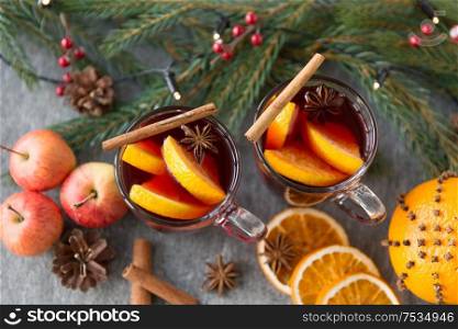 christmas and seasonal treats concept - glass of hot mulled wine with orange slice, apples and fir branch on grey background. glass of hot mulled wine, cookies, apples and fir