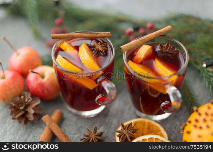 christmas and seasonal treats concept - glass of hot mulled wine with orange slice, apples and fir branch on grey background. glass of hot mulled wine, cookies, apples and fir