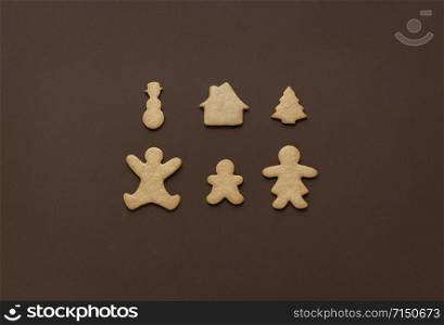 Christmas as family time concept with gingerbread cookies in shape of parents and child, and Xmas symbols, on a brown background. Traditional sweets.