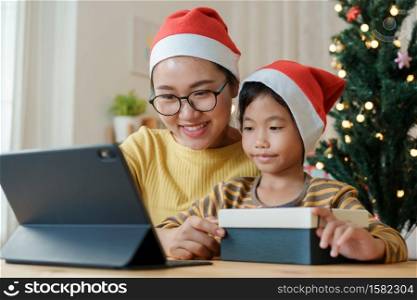 Christmas. Asian family with a mother and daughter giving gift box via video call together with tablet at home