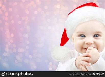 christmas, babyhood, childhood and people concept - happy baby in santa hat over rose quartz and serenity lights background
