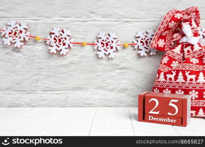 Christmas background, red gift bag and red wooden perpertual calendar on white wooden background. Top view, flat lay with copy space, banner, header, New Year concept. Cristmas background with red gift bag and perpertual wooden calendar on white wooden background.