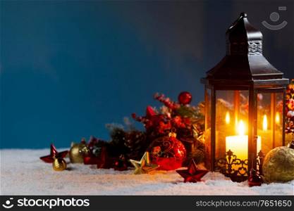 Christmas background with burning candle inside lantern and bauble decorations in snow. Christmas lantern and decorations