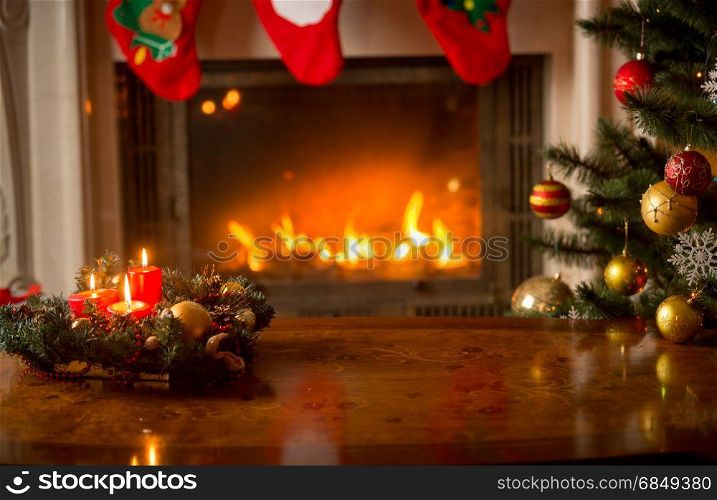Christmas background with burning candles on wooden table in front of fireplace and Christmas tree