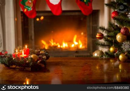Christmas background with burning candles on wooden table in front of fireplace and Christmas tree