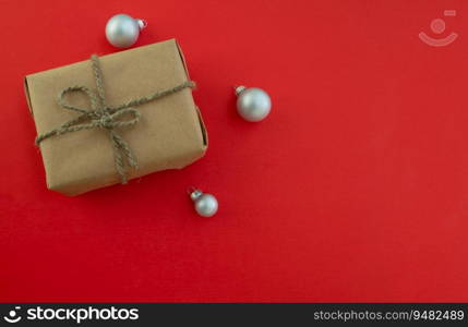 Christmas background with copy space. A gift in craft paper and Christmas balls on a red background. Festive background.