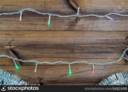 Christmas background with copy space in the center. Silver tinsel and garland on a wooden background. Festive background.