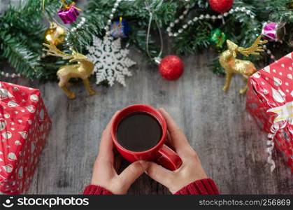 Christmas background with decorations and gift boxes on wooden board.The woman is holding in her hand a red cup.