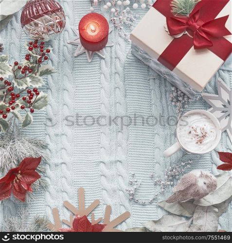 Christmas background with gift box, mug of hot chocolate, burning candle and festive decoration on light blue knitted blanket. Top view. Holiday flat lay. Frame