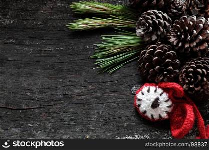 Christmas background with pine cone, green leaf and red clock on black wooden background