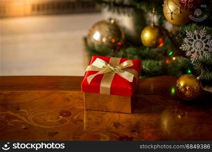 Christmas background with red gift box on wooden table in front of burning fireplace and Christmas tree