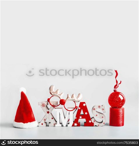 Christmas background with Santa hut, word Xmas, candles and red holiday ball stand on light gray background. Modern still life. Copy space. Festive greeting card
