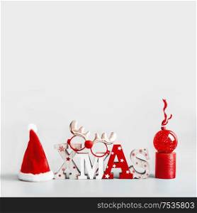 Christmas background with Santa hut, word Xmas, candles and red holiday ball stand on light gray background. Modern still life. Copy space. Festive greeting card