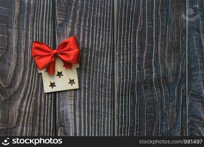 Christmas background with wooden decorative gift and red bow on the old wooden board Copy space. Christmas background with wooden decorative gift and red bow on the old wooden board