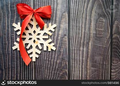 Christmas background with wooden snowflake and red bow on the old wooden board. Copy space. Christmas background with wooden snowflake and red bow on the old wooden board
