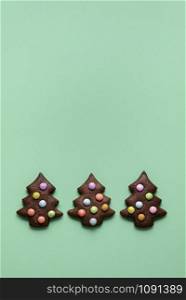 Christmas baking banner with three chocolate gingerbread cookies, Christmas tree shape, decorated with smarties, on a green background. Above view.