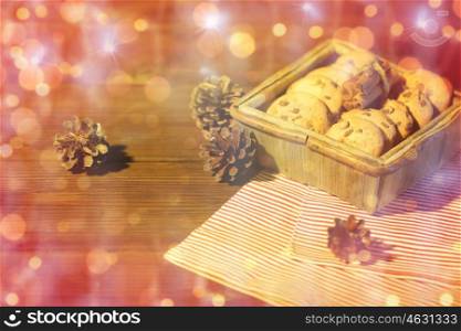christmas, baking, culinary, holidays and food concept - close up of oat cookies in wooden box with cinnamon and pinecones on table over lights