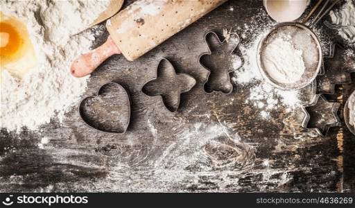 Christmas baking: flour, egg yolk, rolling pin, cookie cutters on dark wooden background, top view, border