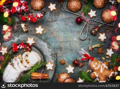 Christmas baking sweet food frame with homemade gingerbread man, cookies, stollen with spices , fir branches and red holiday decoration on dark rustic background, top view