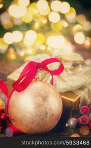 christmas ball with red ribbon and gift box with christmas lights in background, retro toned
