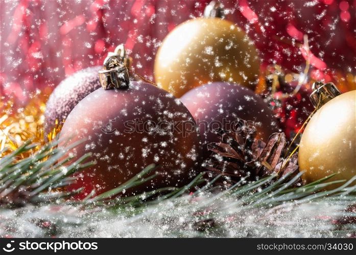 Christmas balls on fir branches covered with snow and Falling snowflakes. Christmas balls lying on spruce branches. Blurred background and falling snowflakes