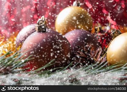 Christmas balls on fir branches covered with snow and Falling snowflakes. Christmas balls lying on spruce branches. Blurred background and falling snowflakes