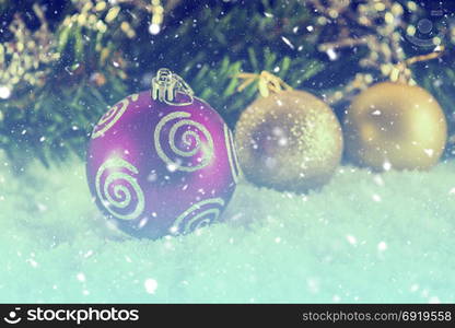 Christmas balls on snow against the background of blurred Christmas tree branches and falling snow