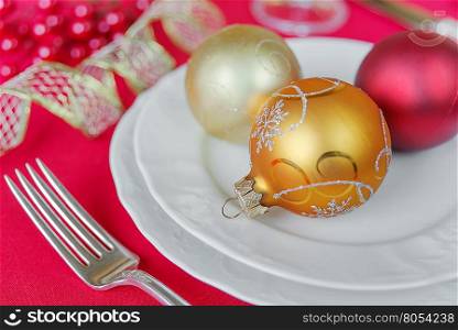 Christmas balls on the white porcelain plate and silver fork located on the red tablecloth