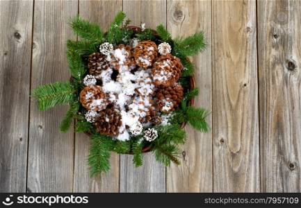 Christmas basket filled with pine tree branches, cones and snow on rustic wooden boards.
