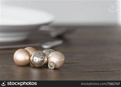 Christmas baubles in elegant colors on a dinner table with dish in the background