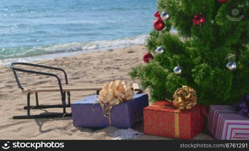 Christmas beach holidays - decorated tree with gift boxes and sledge