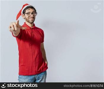 Christmas bearded man standing pointing at you isolated. Friendly guy in christmas hat with hands in his pocket pointing at you, Isolated christmas man pointing at you isolated