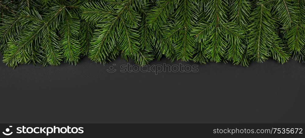 Christmas border arranged with fresh fir branches and pine cone on black paper background , copy space for text. Christmas border of fir branches