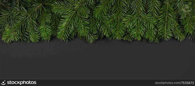 Christmas border arranged with fresh fir branches and pine cone on black paper background , copy space for text. Christmas border of fir branches