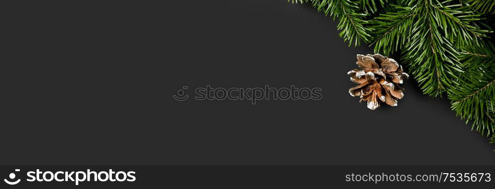 Christmas border arranged with fresh fir branches and pine cone on black paper background , copy space for text. Christmas border of fir branches